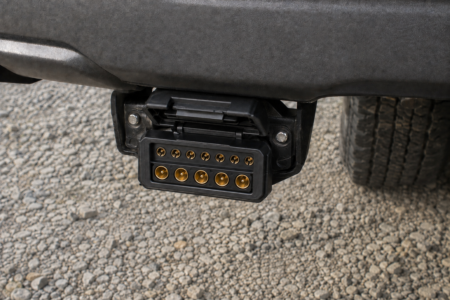 12-pin flat trailer socket with its lid open and contacts visible beneath a vehicle bumper
